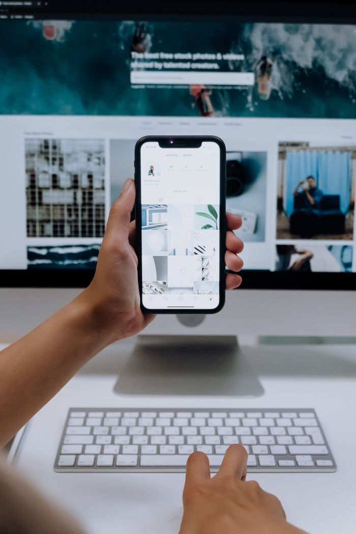 Services Person uses a smartphone in front of a computer screen displaying stock photos, showcasing modern technology use.