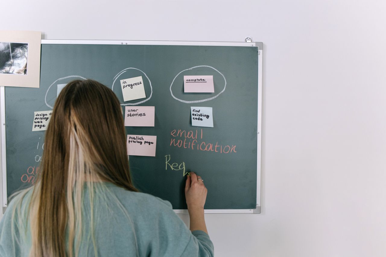 Services A woman writing on a chalkboard with business strategy notes in a modern office environment.