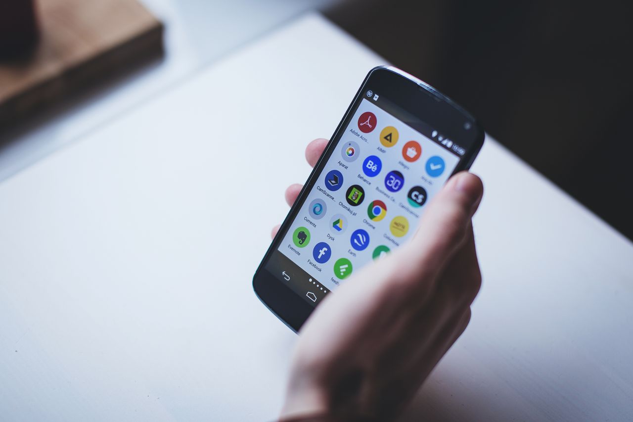 Services Close-up of a person holding a smartphone with various app icons visible on the screen.